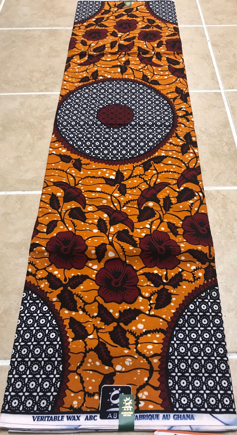 May include: A brown and white patterned fabric with a floral design. The fabric has a repeating pattern of circles with a smaller circle in the center. The fabric is made in Ghana.