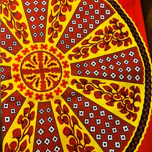 Puede incluir: Una tela amarilla y roja con un patr&oacute;n circular. El patr&oacute;n presenta un c&iacute;rculo central con una forma de cruz y l&iacute;neas radiantes con dise&ntilde;os florales. El fondo es de color rojo s&oacute;lido.