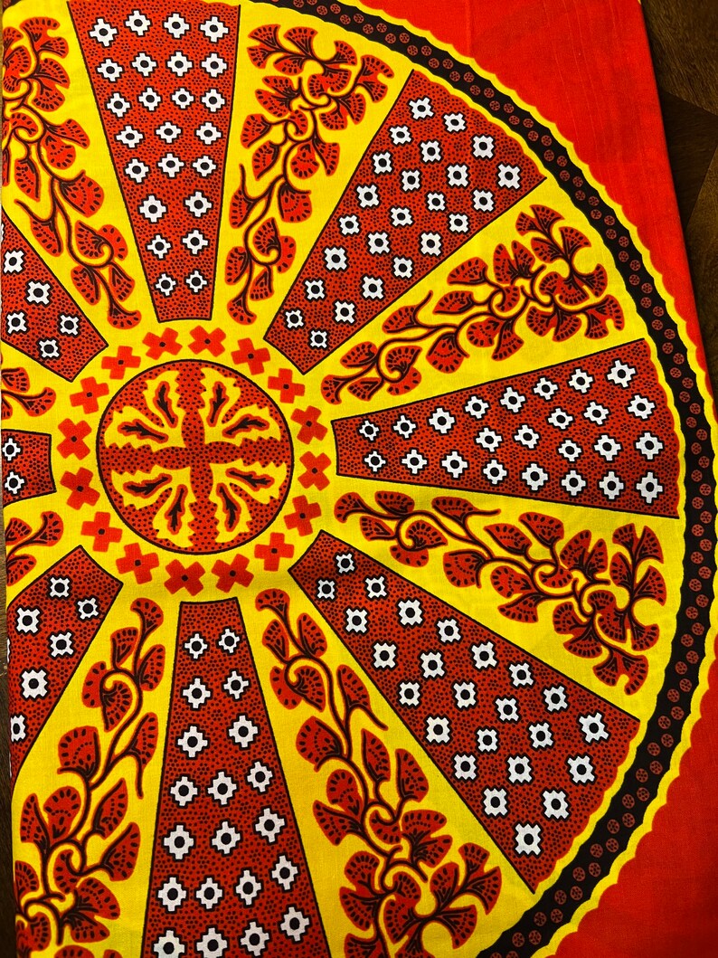 Puede incluir: Una tela amarilla y roja con un patr&oacute;n circular. El patr&oacute;n presenta un c&iacute;rculo central con una forma de cruz y l&iacute;neas radiantes con dise&ntilde;os florales. El fondo es de color rojo s&oacute;lido.