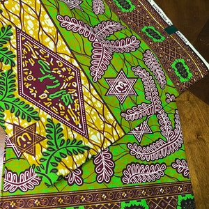 Peut inclure: Tissu vert et marron avec un motif g&eacute;om&eacute;trique compos&eacute; d'&eacute;toiles et de feuilles. Le tissu a une bordure blanche avec le texte "COSTA SHENATON" et "VULCAN" imprim&eacute; dessus.