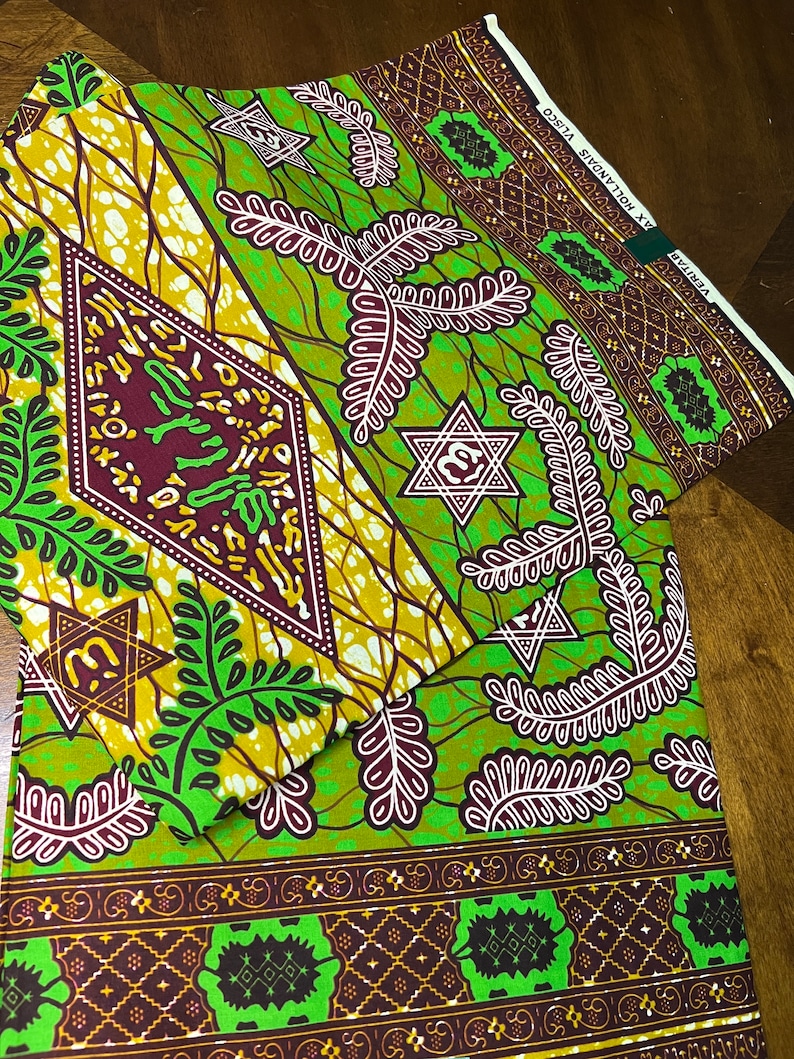 Peut inclure: Tissu vert et marron avec un motif g&eacute;om&eacute;trique compos&eacute; d'&eacute;toiles et de feuilles. Le tissu a une bordure blanche avec le texte "COSTA SHENATON" et "VULCAN" imprim&eacute; dessus.