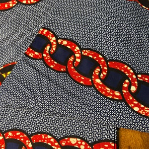 K&ouml;nnte beinhalten: Nahaufnahme eines gemusterten Stoffes mit einem sich wiederholenden Kettendesign in Rot und Wei&szlig; vor einem marineblauen Hintergrund. Der Stoff hat auch ein kleines wei&szlig;es geometrisches Muster. Der Stoff ist gefaltet.