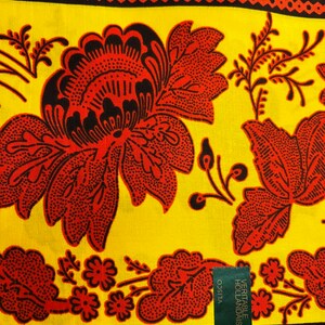 Puede incluir: Una tela amarilla con un patr&oacute;n floral rojo y negro. La tela tiene una etiqueta Vlisco con el texto "VERITABLE HOLLANDAIS".
