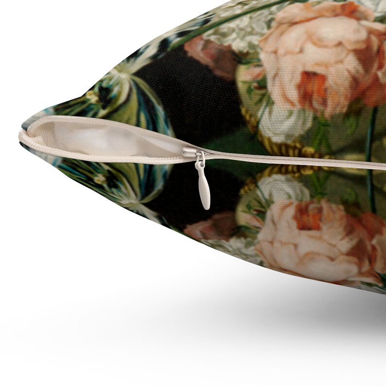 Op de afbeelding: Een close-up van een kussen met een rits. Het kussen heeft een bloemenpatroon met roze, witte en groene bloemen op een donkere achtergrond.