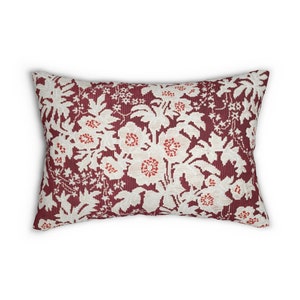 May include: Rectangular decorative pillow with a floral pattern. The pillow features a burgundy background with a repeating pattern of white flowers and red accents. The pillow is a decorative home accent.