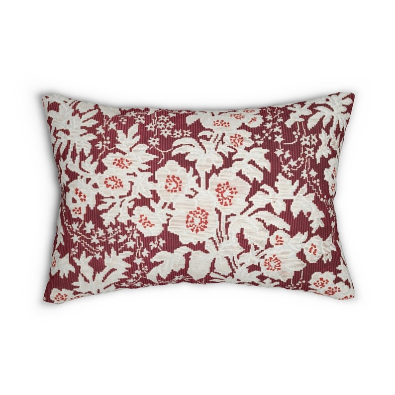 May include: Rectangular decorative pillow with a floral pattern. The pillow features a burgundy background with a repeating pattern of white flowers and red accents. The pillow is a decorative home accent.