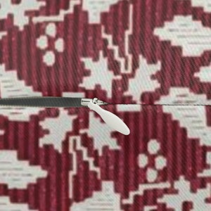 May include: Close-up of a pillow with a burgundy and white geometric pattern. A white zipper pull is visible on the side of the pillow. The pillow has a textured surface.