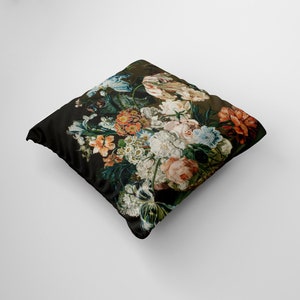 Op de afbeelding: Een zwart kussen met een bloemenprint met verschillende bloemen in tinten roze, rood, wit en blauw. De bloemen zijn in een boeket gerangschikt en lijken in een vintage stijl geschilderd te zijn.