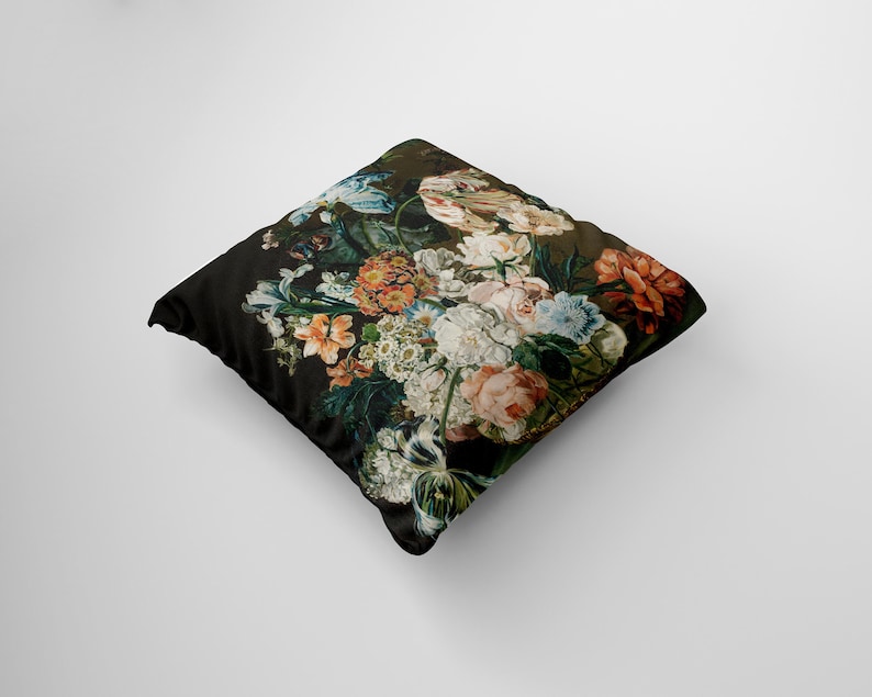 Op de afbeelding: Een zwart kussen met een bloemenprint met verschillende bloemen in tinten roze, rood, wit en blauw. De bloemen zijn in een boeket gerangschikt en lijken in een vintage stijl geschilderd te zijn.