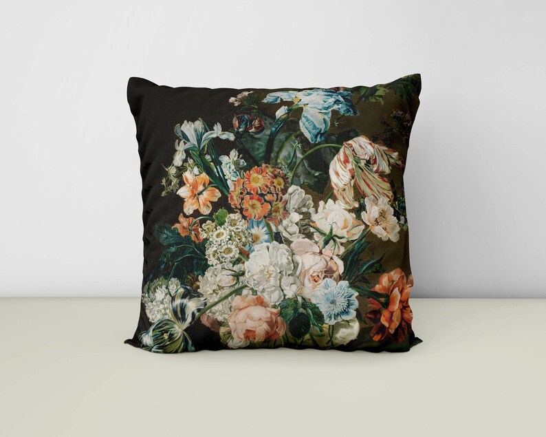 Op de afbeelding: Een zwart kussen met een bloemenprint met verschillende bloemen in tinten roze, rood, wit en geel. De bloemen zijn in een boeket gerangschikt en zijn geplaatst tegen een donkergroene achtergrond.