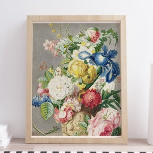 Op de afbeelding: Een ingelijste bloemenprint met een levendig boeket bloemen in een decoratieve vaas. Het kunstwerk toont een verscheidenheid aan bloemen in tinten geel, wit, rood, roze en blauw, tegen een grijze achtergrond. De lijst is van lichtgekleurd hout.