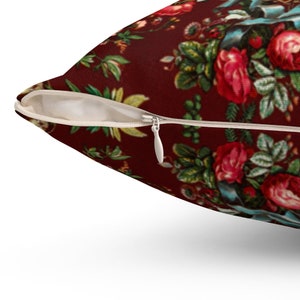 May include: A red pillow with a floral pattern featuring roses, leaves, and a blue ribbon. The pillow has a zipper closure.
