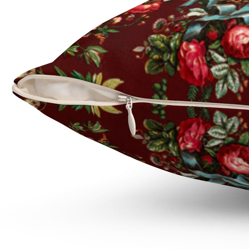 May include: A red pillow with a floral pattern featuring roses, leaves, and a blue ribbon. The pillow has a zipper closure.