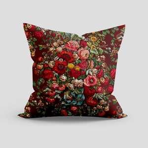 May include: A red pillow with a floral pattern featuring a bouquet of red, pink, and yellow flowers. The flowers are surrounded by green leaves and vines.