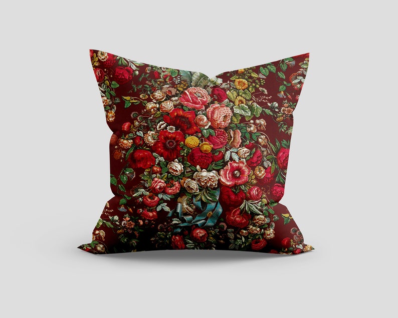 May include: A red pillow with a floral pattern featuring a bouquet of red, pink, and yellow flowers. The flowers are surrounded by green leaves and vines.