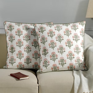 May include: Two decorative throw pillows with a floral pattern. The pillows have a white background with a repeating design of pink flowers and green leaves. The pillows are edged with a green trim.