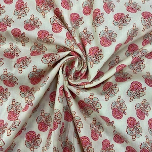 May include: Cream-colored fabric with a repeating floral pattern in shades of pink, red, and light blue. The fabric is folded, showing the texture and design of the printed pattern. The floral design is a paisley-like motif.