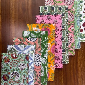 Puede incluir: Una colecci&oacute;n de servilletas de tela plegadas con varios estampados florales. Las servilletas presentan una gama de colores, incluyendo verde, rosa, naranja y azul, con dise&ntilde;os intrincados. Las servilletas est&aacute;n dispuestas en una fila diagonal, mostrando los diferentes patrones.