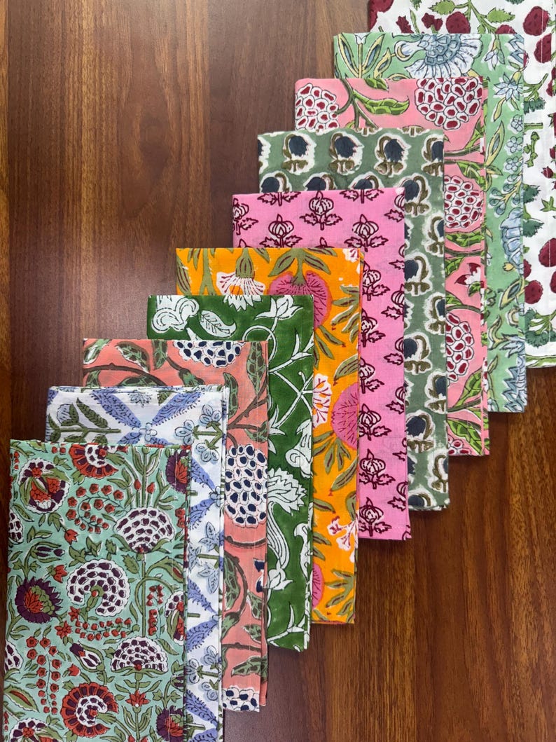 Puede incluir: Una colecci&oacute;n de servilletas de tela plegadas con varios estampados florales. Las servilletas presentan una gama de colores, incluyendo verde, rosa, naranja y azul, con dise&ntilde;os intrincados. Las servilletas est&aacute;n dispuestas en una fila diagonal, mostrando los diferentes patrones.