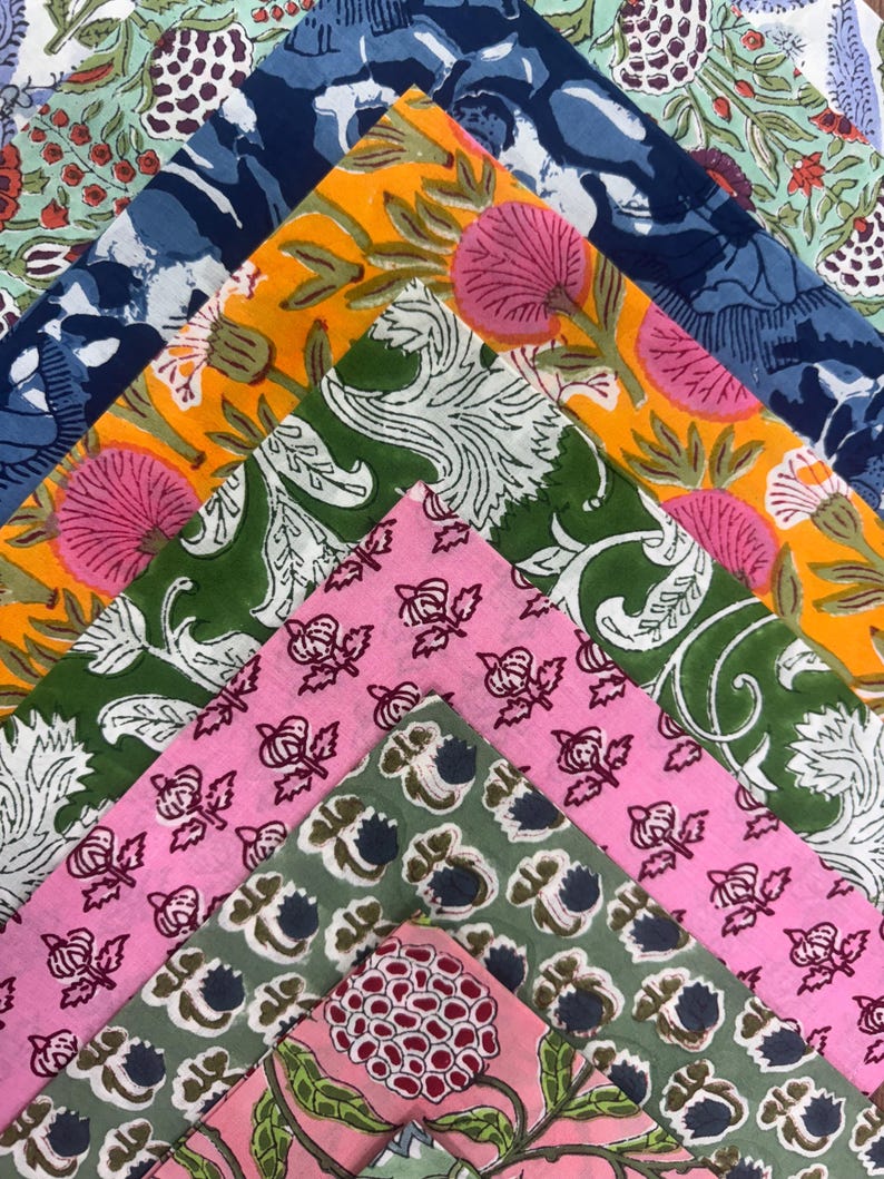 Puede incluir: Una colecci&oacute;n de cuadrados de tela plegados en varios colores y estampados florales. Las telas incluyen tonos de azul, amarillo, verde y rosa, con dise&ntilde;os que presentan flores grandes y motivos de hojas intrincados. La disposici&oacute;n muestra la variedad de estampados.