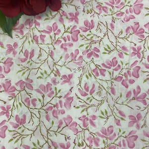 May include: White fabric featuring a repeating pattern of pink flowers and green leaves on brown stems. A large, dark red flower is in the upper left corner. The floral design is suitable for textiles or home decor.