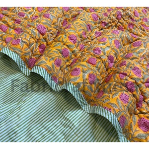 May include: A quilted blanket with a vibrant floral pattern in shades of yellow and pink. The reverse side features green and white stripes. The edges are scalloped, adding a decorative touch to this bedding item.
