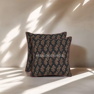 May include: Two square throw pillows with a dark background and a repeating pattern of brown floral shapes. The pillows have a red border and the text "FABRICRAFTINDIA" is visible on the front.