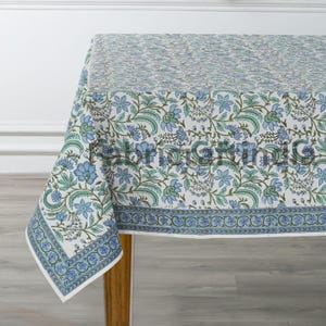 May include: A white tablecloth with a blue and green floral pattern. The tablecloth has a border with a repeating pattern of blue and green.