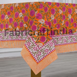 May include: Orange floral tablecloth with a repeating pattern of pink flowers and green leaves. The border features a white and pink floral design with orange stripes. The tablecloth is made of a soft fabric.