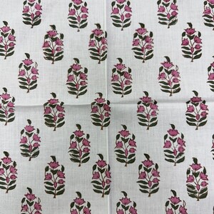 May include: White fabric with a repeating pattern of pink floral designs. Each floral element features a cluster of pink blossoms atop a stem with green leaves. The pattern is evenly spaced across the fabric.