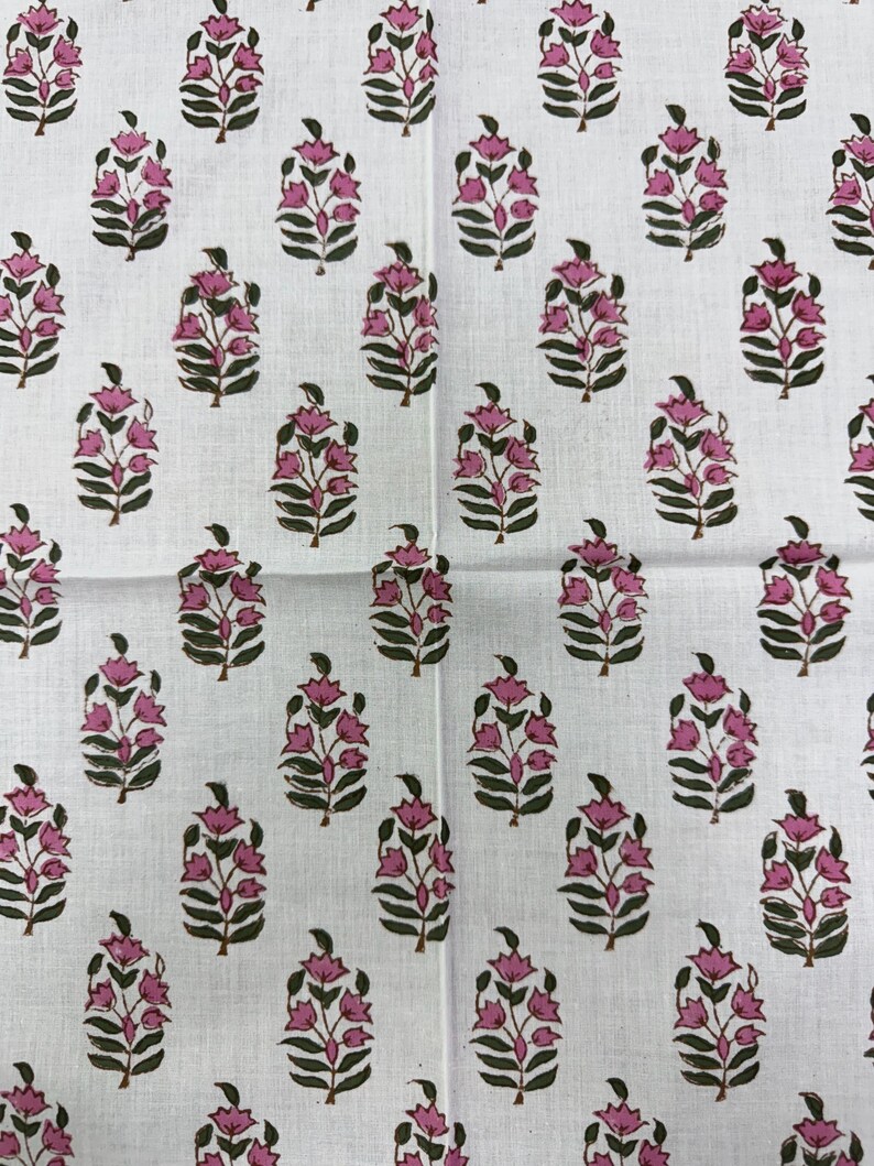 May include: White fabric with a repeating pattern of pink floral designs. Each floral element features a cluster of pink blossoms atop a stem with green leaves. The pattern is evenly spaced across the fabric.