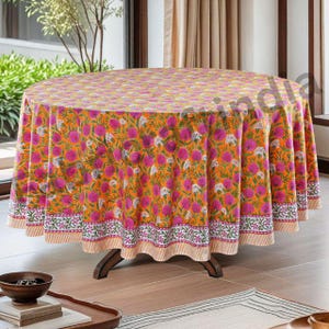 Puede incluir: Un mantel redondo de color naranja y rosa con un diseño floral y un borde blanco. El mantel está hecho de algodón y tiene un diseño tradicional indio.