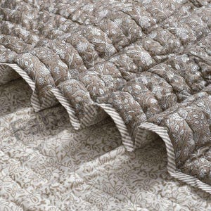Peut inclure: Une couverture matelassée avec un motif floral dans les tons taupe et blanc. Les bords sont finis avec une bordure rayée. Le design est de style classique et élégant.