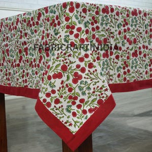 May include: A white tablecloth with a repeating pattern of red cherries and green leaves. The tablecloth has a solid red border. The text "FABRIC CRAFT IN INDIA" is printed on the tablecloth.