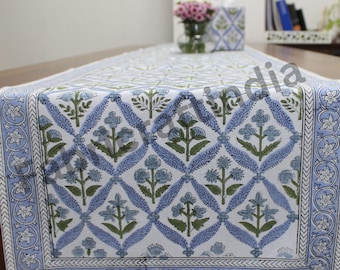 May include: A blue and white table runner with a floral pattern. The runner has a white background with blue and green floral designs. The runner has a blue border with a white floral design.