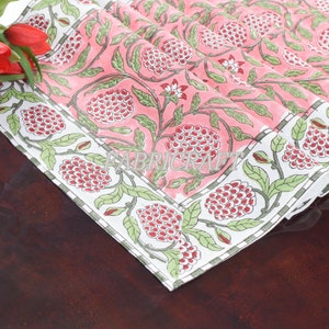 May include: Pink cotton table runner with a white border and a floral pattern featuring green leaves and red flowers. The pattern is repeated throughout the runner.