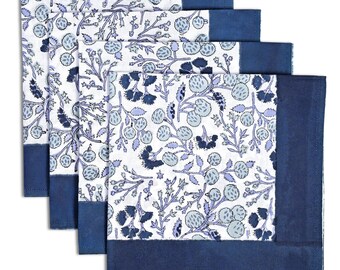 May include: Four white cloth napkins with a floral pattern in shades of blue and gray. Each napkin has a solid navy blue border along one edge. The floral design features stylized berries and branches.