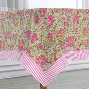 May include: A green tablecloth with a pink floral pattern and a pink and white striped border. The tablecloth is laid out on a table.