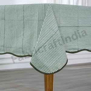 May include: Green and white striped tablecloth with a scalloped edge. The tablecloth is made of cotton and has a casual, farmhouse style.