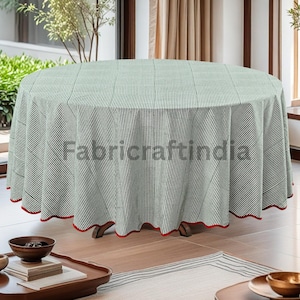 May include: A round tablecloth featuring a green and white striped design. The tablecloth has a scalloped red trim. The tablecloth is draped over a wooden table. The image is taken in a well-lit room.