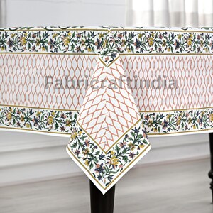 May include: White rectangular tablecloth with a repeating peach-colored diamond pattern in the center. The border features a floral design with yellow, green, and blue accents. The text "Fabricraftindia" is printed on the tablecloth.