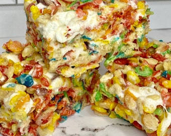 May include: A stack of three colorful cereal treats with marshmallow and cereal pieces. The treats are a light brown color and have a white marshmallow layer in the middle.