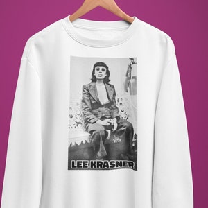 May include: White sweatshirt featuring a black and white photograph of a person wearing sunglasses and a suit, seated on a sofa. The text "LEE KRASNER" is printed beneath the image.