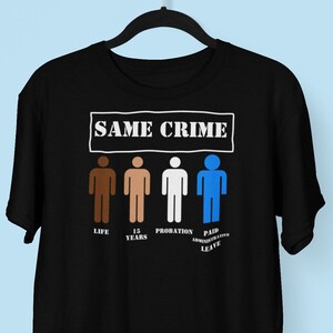 Può includere: Maglietta nera con il testo "SAME CRIME" in lettere bianche. Sotto il testo sono mostrate quattro figure stilizzate, ciascuna con un diverso tono di pelle. Le figure stilizzate sono etichettate come "LIFE", "15 YEARS", "PROBATION" e "PAID ADMINISTRATIVE LEAVE".