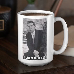 May include: White ceramic mug with a black and white photo of Juan Rulfo, a Mexican writer, on the front. The mug has a black handle and is filled with coffee.