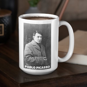 May include: White ceramic mug with a black and white photo of Pablo Picasso on it. The mug has a black handle and the text "PABLO PICASSO" is printed on the bottom.