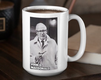 May include: White ceramic mug with a black and white photo of John D. Macdonald. The mug has a handle and is filled with coffee.