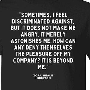 May include: Black t-shirt with a white quote by Zora Neale Hurston: "Sometimes, I feel discriminated against, but it does not make me angry. It merely astonishes me. How can any deny themselves the pleasure off my company? It is beyond me."