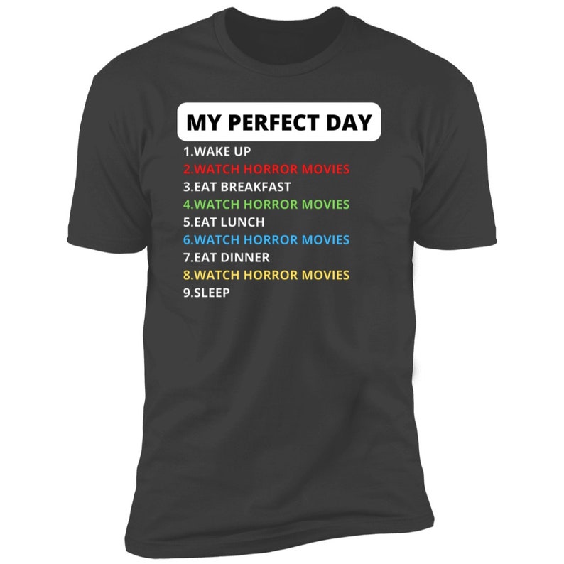 May include: A dark grey t-shirt with the text "MY PERFECT DAY" in white. The text is followed by a list of activities, including "WATCH HORROR MOVIES" in different colours.