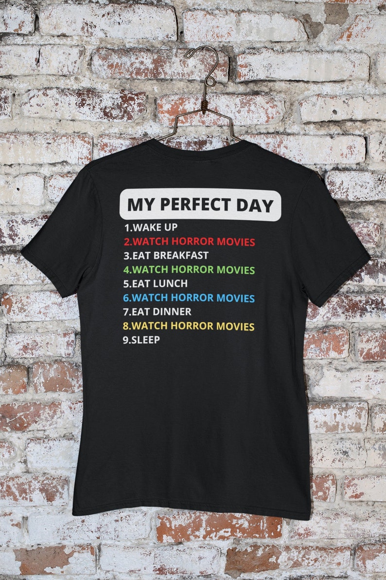 May include: Black t-shirt with white text that reads "My Perfect Day" and a list of activities, including "Watch Horror Movies" repeated multiple times.